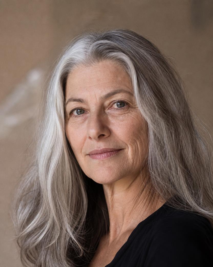 Mulher de cerca de 55 anos com cabelo longo grisalho prateado, brilho natural alto e expressão serena.
